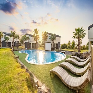 A swimming pool with lounge chairs, palm trees, and modern buildings in the background. - Pool & Villa Sorang (Jeju City)