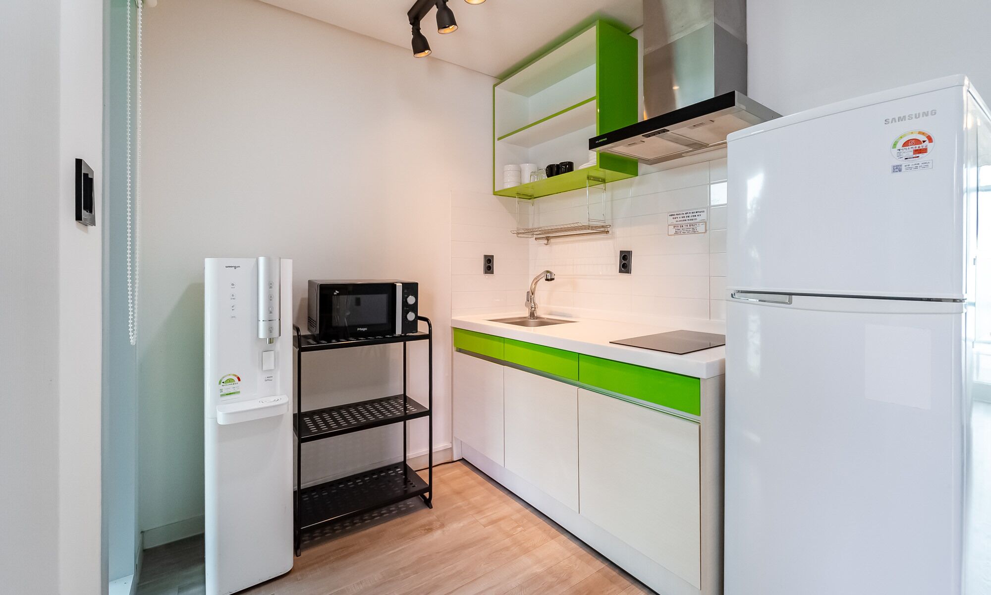 A compact kitchen with a white refrigerator, a microwave, a sink, and a green countertop.