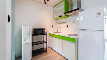 A compact kitchen with a white refrigerator, a microwave, a sink, and a green countertop.