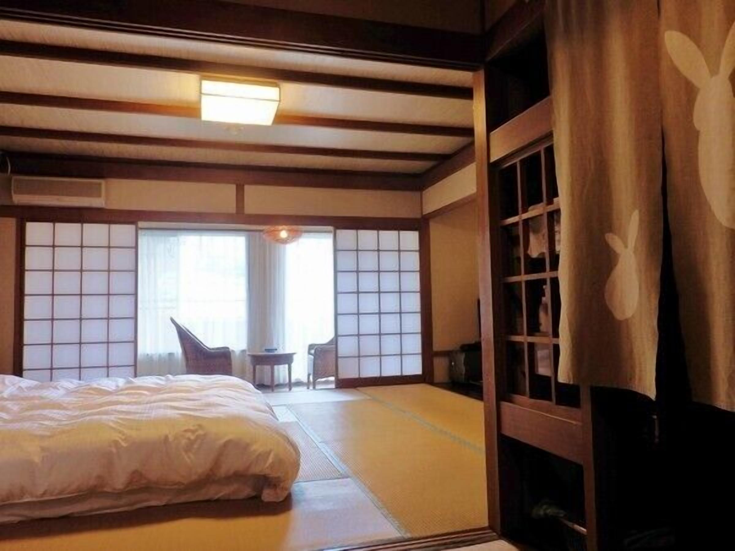 A traditional Japanese room with tatami flooring, a bed, a small table, and sliding doors.