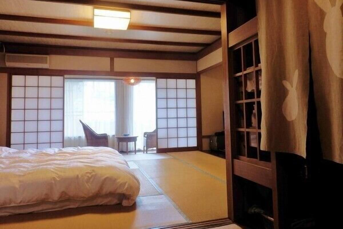 Um quarto japonês tradicional com tatames, uma cama, uma pequena mesa e portas deslizantes.