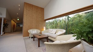 A modern living room with a sofa, chairs, and a coffee table. There is a large window with a view of greenery outside. - Breezbay Shuzenji Hotel (Izu)