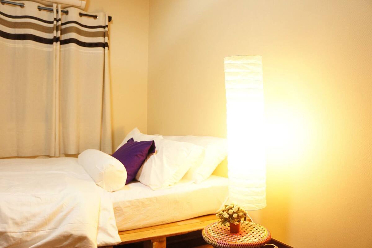 A bedroom with a bed, a bedside table with a lamp, and curtains.