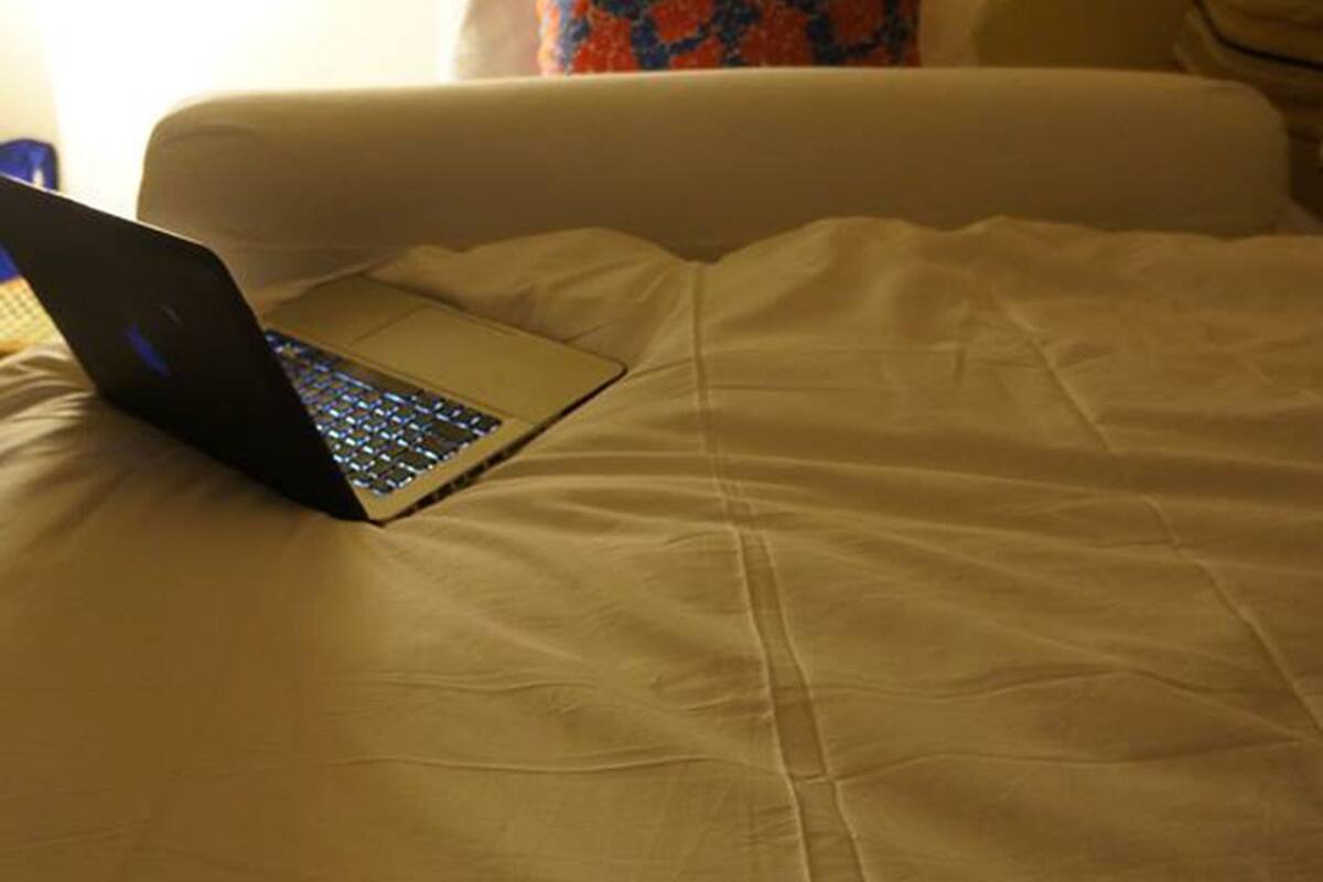 A bed with a laptop on it, a pillow with a blue and orange pattern, and a lamp in the background.