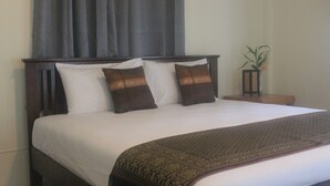 A neatly made bed with white and brown bedding, a dark headboard, and a small table with a plant beside it. - Privacy Resort Koh Chang (Ko Chang)
