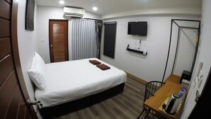 A hotel room with a bed, a desk, a chair, a TV, and a mirror. - The Ghee House (Chiang Mai)