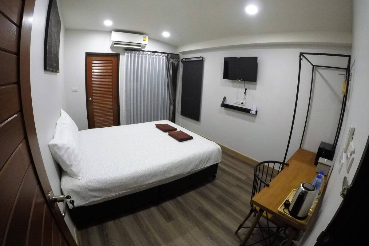 A hotel room with a bed, a desk, a chair, a TV, and a mirror.