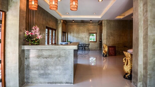 A reception area with a concrete counter, hanging wicker lamps, and a large golden statue. - The Ghee House (Chiang Mai)
