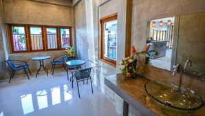 A modern bathroom with a glass sink, a large mirror, and a seating area with chairs and a table. - The Ghee House (Chiang Mai)