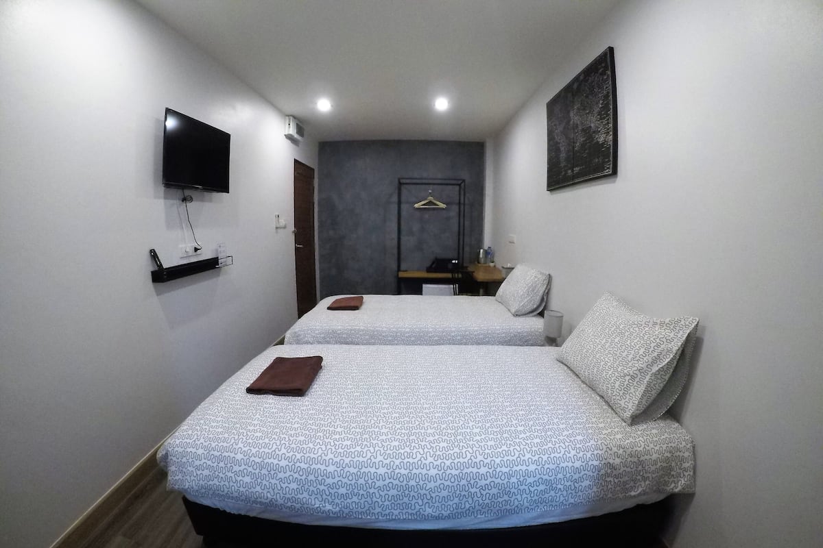 A hotel room with two beds, a flat-screen TV mounted on the wall, a small table with a chair, and a door leading to a bathroom.
