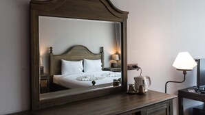 Ein Hotelzimmer mit einem großen Spiegel, einem Bett mit weißer Bettwäsche, einem Nachttisch mit einer Lampe und einem kleinen Tisch mit einer Karaffe und Tasse.