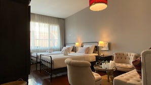 Ein Hotelzimmer mit einem Bett, zwei Nachttischen, einem Sessel, einer Couch, einer Hängelampe und einem Fenster mit Vorhängen.