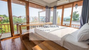 Un dormitorio amplio con una cama grande, suelo de madera y un balcón con vistas a zonas verdes y edificios.