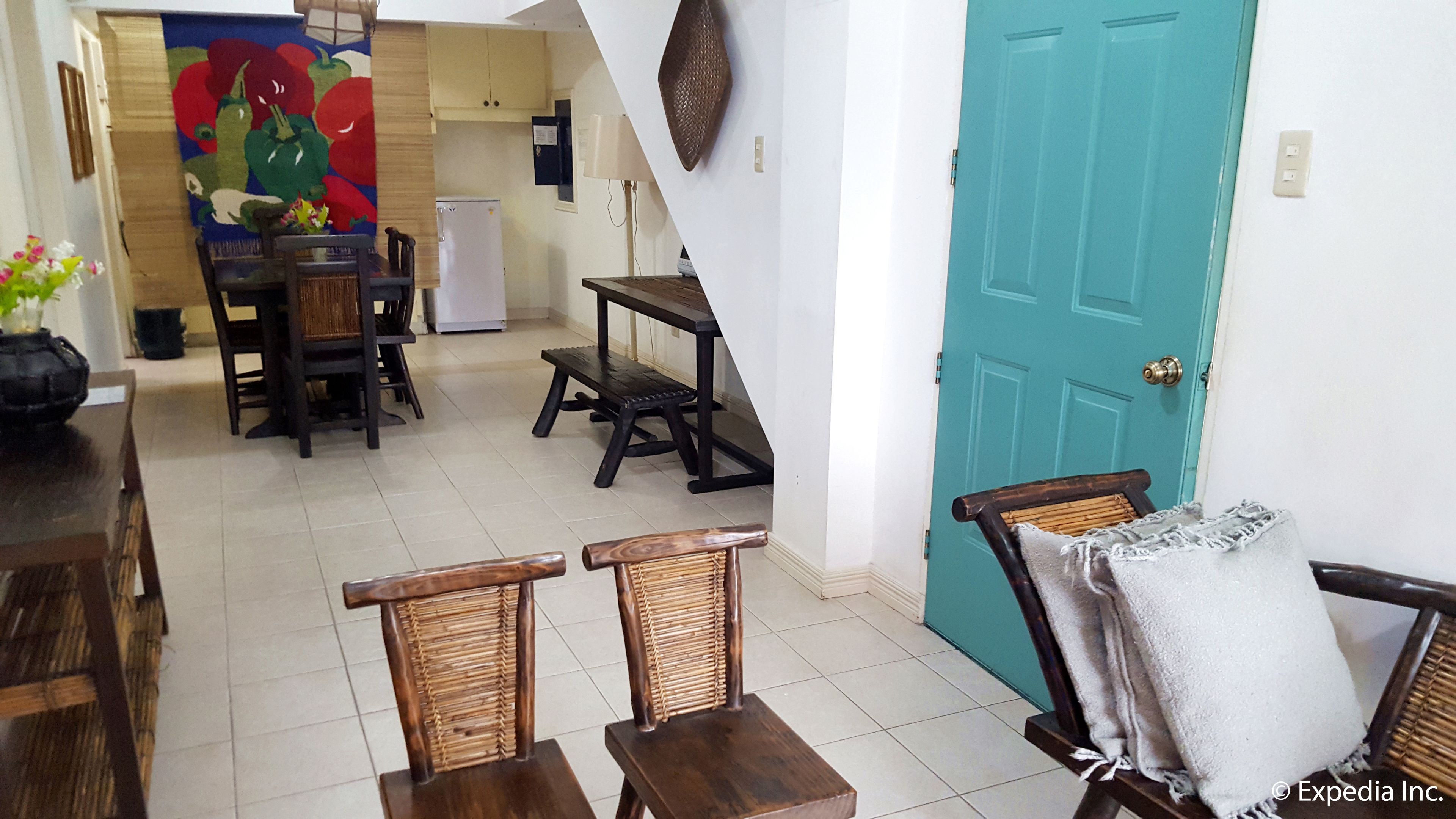 A dining area with a table and chairs, a kitchen in the background, and a teal door.