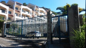 A gated entrance with a stone pillar, a car parked inside, and a multi-story building with balconies in the background. - Baguio Vacation Apartments (Baguio)