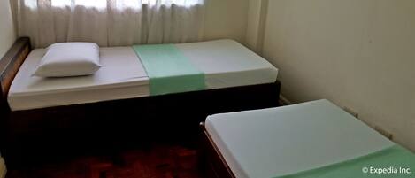 Una habitación pequeña con cama individual, cabecera de madera, colcha verde y almohada blanca.