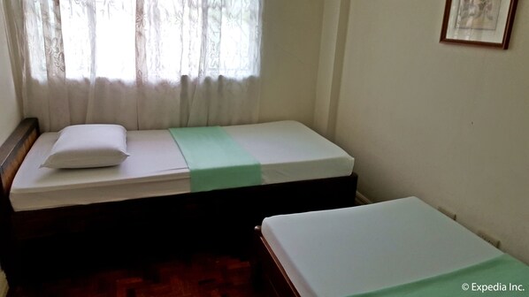 A small, single-bed room with a wooden headboard, a green bedspread, and a white pillow.