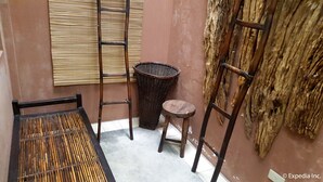 A small room with a bamboo mat table, a wicker trash bin, a wooden stool, and a metal ladder leaning against the wall. - Baguio Vacation Apartments (Baguio)