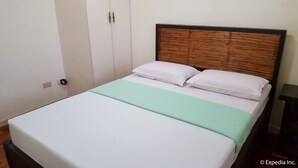 A bed with a wooden headboard, white bedding, and a green throw blanket. - Baguio Vacation Apartments (Baguio)