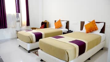 A hotel room with two beds, each with a beige and purple bedspread, and a small bedside table with a lamp.