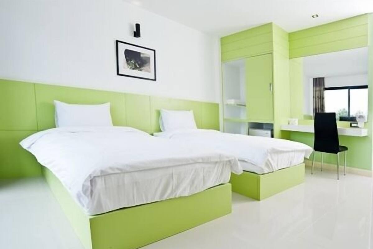 Une chambre d’hôtel moderne avec deux lits, un mur d’accent vert, un bureau avec une chaise et une grande fenêtre.