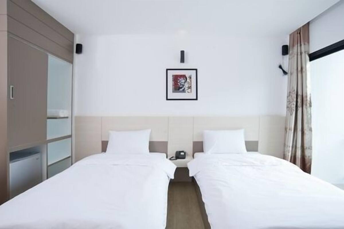Une chambre d’hôtel avec deux lits simples, une table de chevet avec un téléphone, un tableau encadré au mur et une armoire.