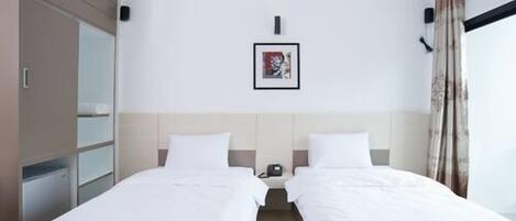 A hotel room with two single beds, a bedside table with a phone, a framed picture on the wall, and a wardrobe.