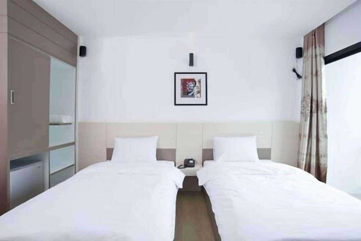 Habitación de hotel con dos camas, un armario, una mesita de noche con teléfono y un cuadro en la pared.