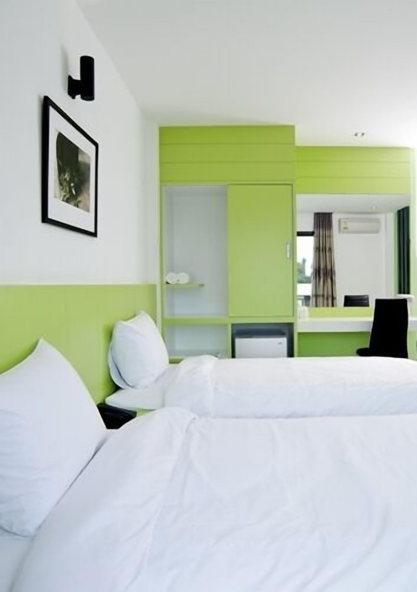Une chambre d’hôtel avec un lit, un bureau et une chaise. Il y a un tableau au mur et une fenêtre avec des rideaux.