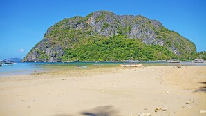A beach with a large mountain in the background, boats on the water, and a clear sky. - Last Frontier Beach Resort - Adults Only (El Nido)