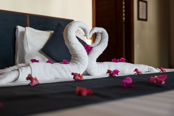 A bed with a towel arranged in the shape of a heart, surrounded by pink flower petals.