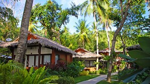 A tropical resort with thatched-roof cottages, lush greenery, and a paved pathway. - Last Frontier Beach Resort - Adults Only (El Nido)