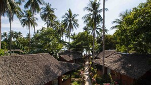 A row of thatched-roof huts with a pathway between them, surrounded by lush greenery and palm trees. - Last Frontier Beach Resort - Adults Only (El Nido)