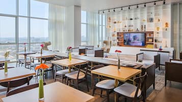 Un comedor moderno con mesas, sillas, un televisor y una estantería con diversos objetos.