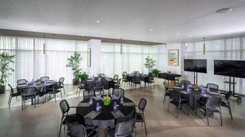 A modern conference room with round tables, black chairs, and large windows with sheer curtains.