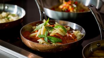 A kitchen with a stove, a pan of pasta, and a bowl of vegetables.