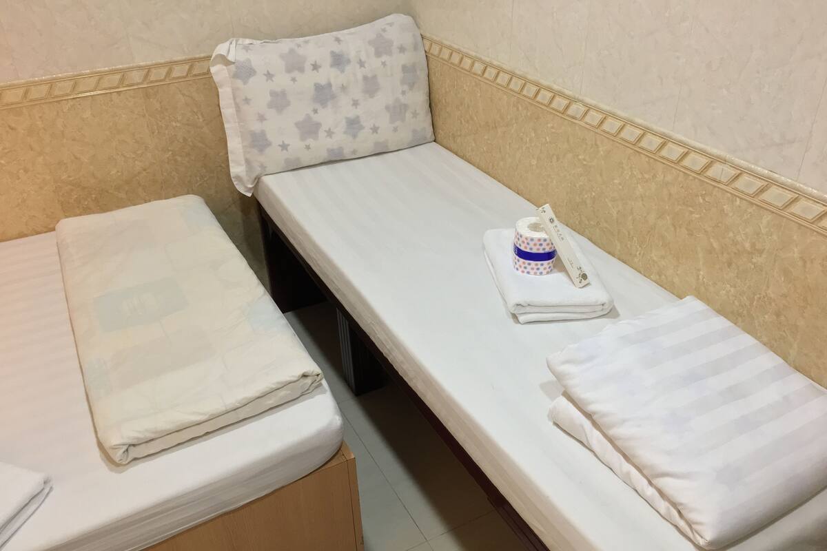 A single bed with a white mattress and a pillow with a star pattern. A roll of toilet paper and a folded towel are on the bed.