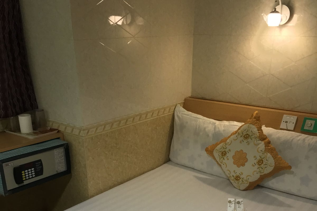 A hotel room with a neatly made bed, a bedside table with a remote control, and a wall-mounted light fixture.