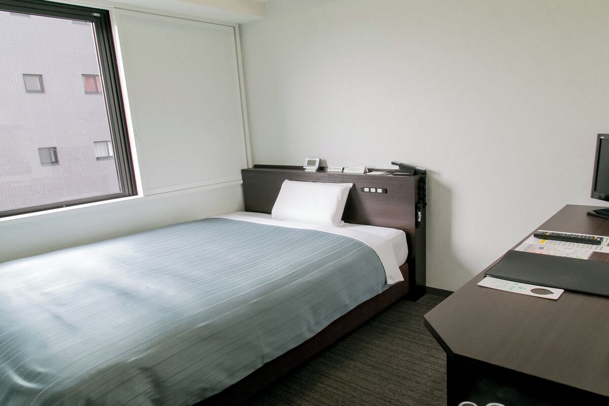 Une chambre d’hôtel avec un lit, un bureau, une chaise, une fenêtre et un téléviseur.
