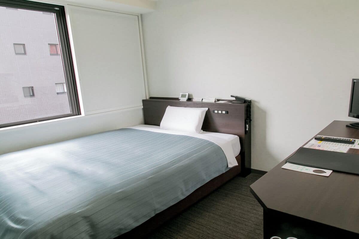 Une chambre d’hôtel avec un lit, un bureau, une chaise, une fenêtre et un téléviseur.