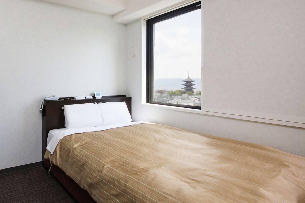 Un lit simple avec une tête de lit en bois, une fenêtre donnant sur une pagode et un mur sobre.