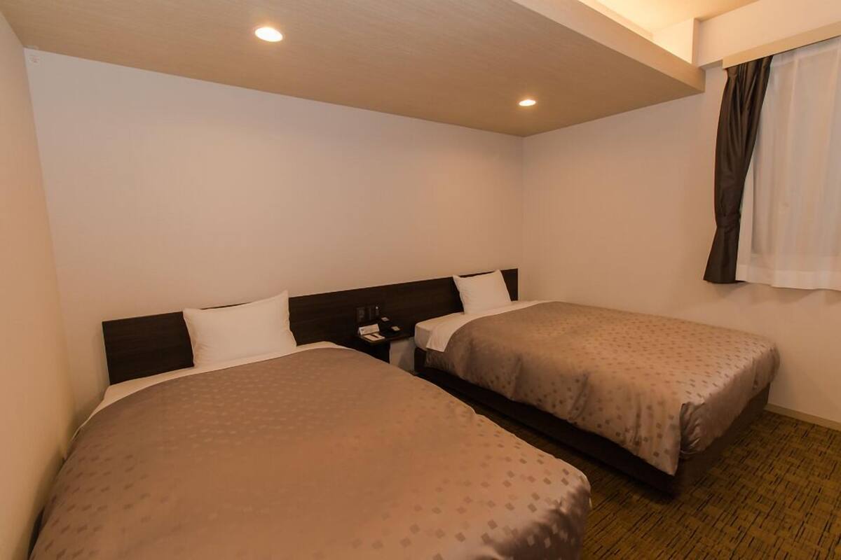 Une chambre d’hôtel avec deux lits, une table de chevet, une fenêtre avec des rideaux et un plancher en bois.