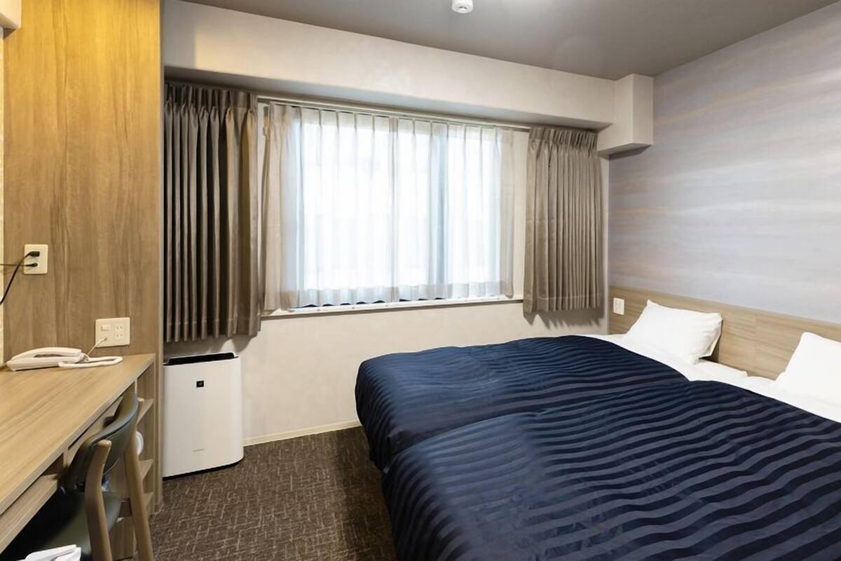 Een hotelkamer met een bed, een bureau, een telefoon en een raam met gordijnen.