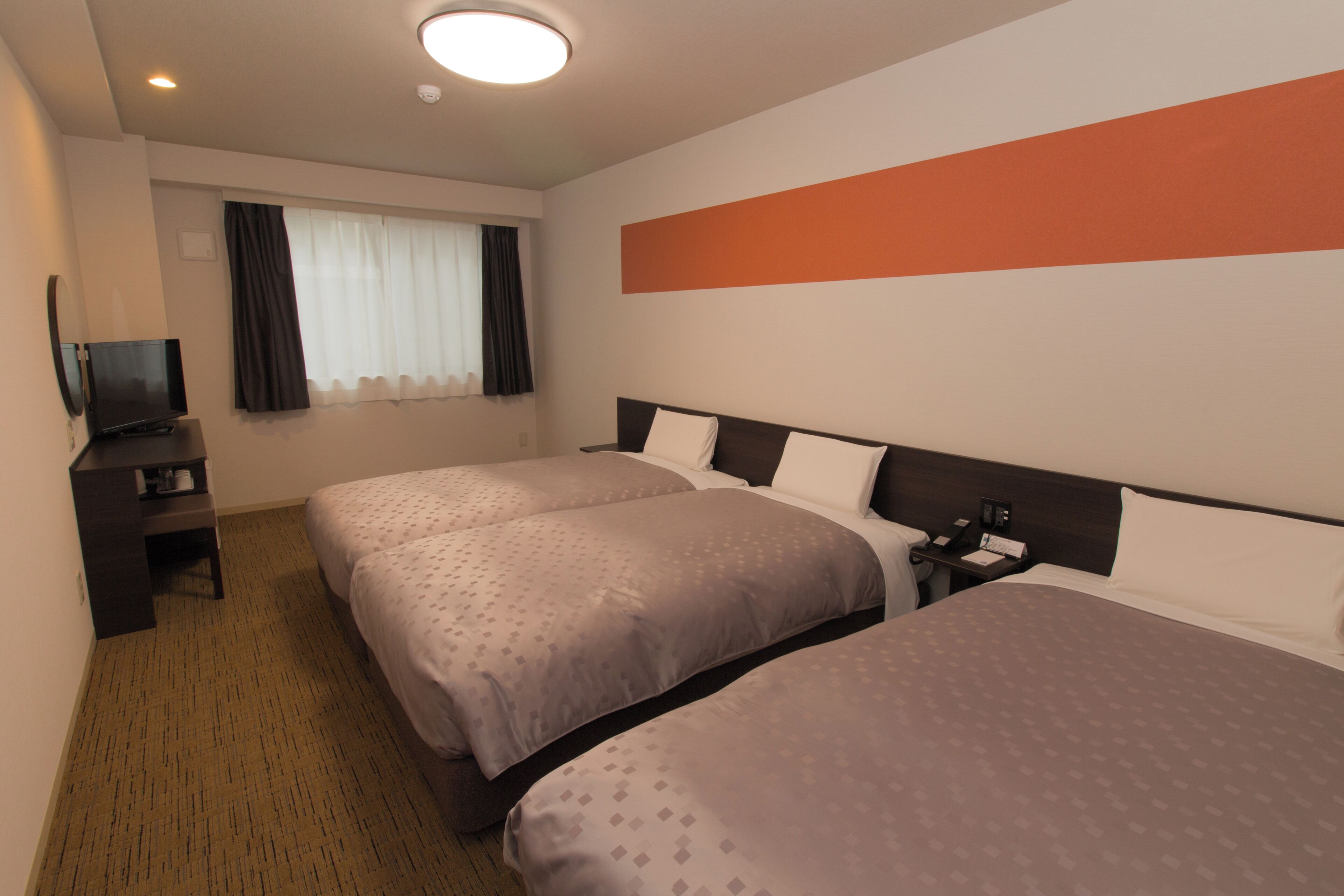 Une chambre d’hôtel avec deux lits, une télévision, un bureau et une fenêtre avec des rideaux.