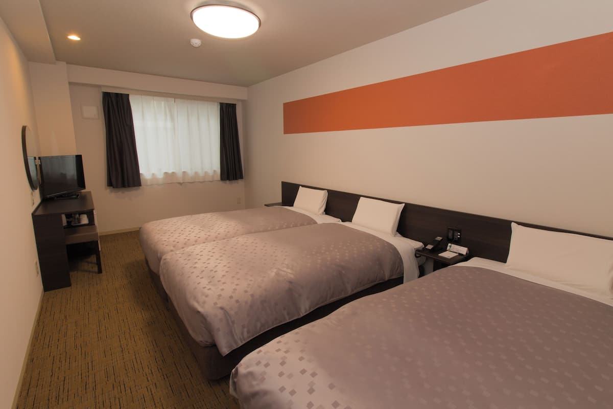 Une chambre d’hôtel avec deux lits, une télévision, un bureau et une fenêtre avec des rideaux.