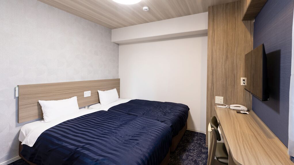 Une chambre d’hôtel équipée d’un lit, d’un bureau, d’une chaise, d’un téléviseur à écran plat fixé au mur et d’un téléphone sur le bureau.