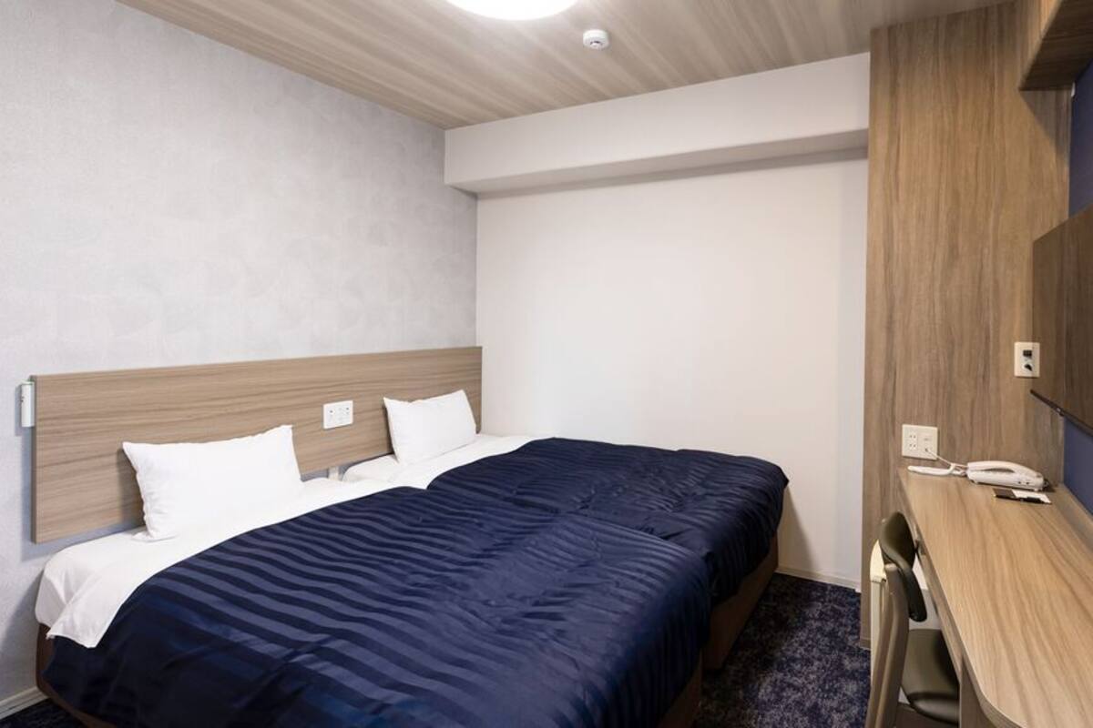 Une chambre d’hôtel équipée d’un lit, d’un bureau, d’une chaise, d’un téléviseur à écran plat fixé au mur et d’un téléphone sur le bureau.