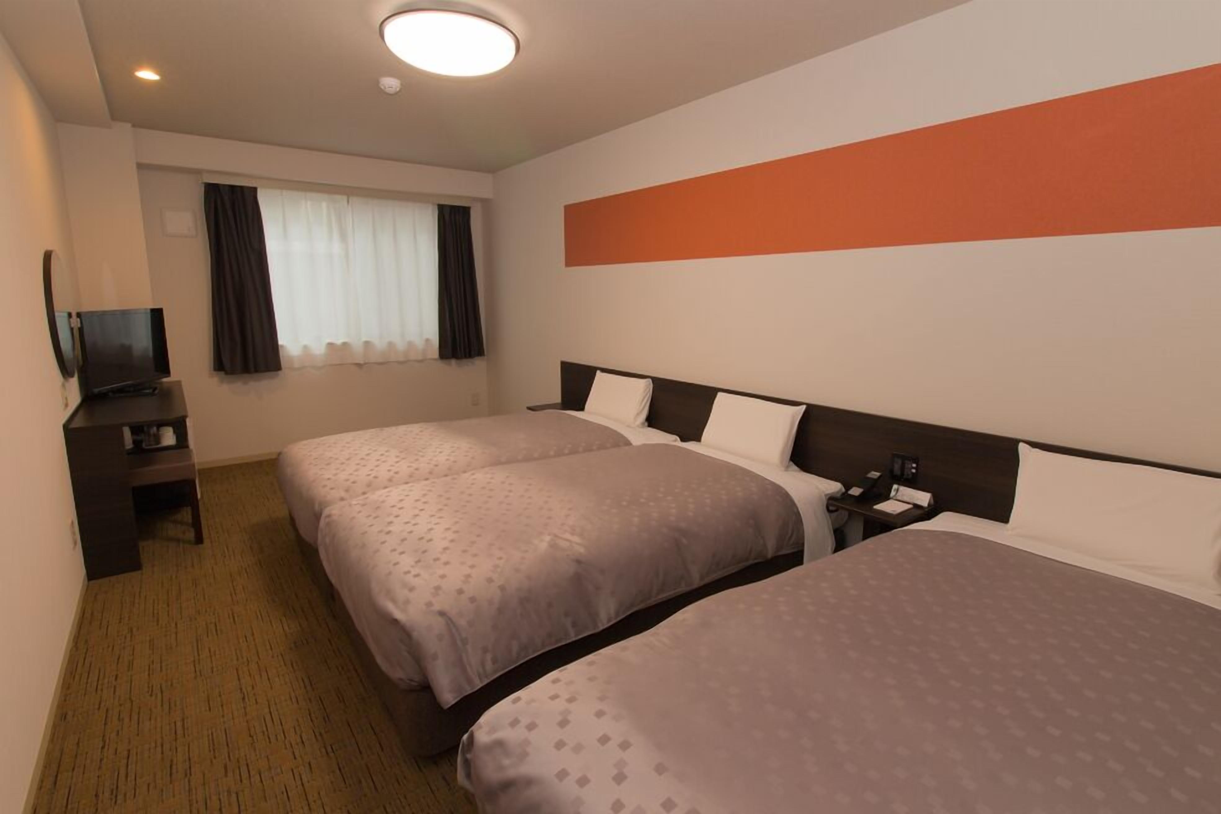 Une chambre d’hôtel avec deux lits, une télévision, un bureau et une fenêtre avec des rideaux.