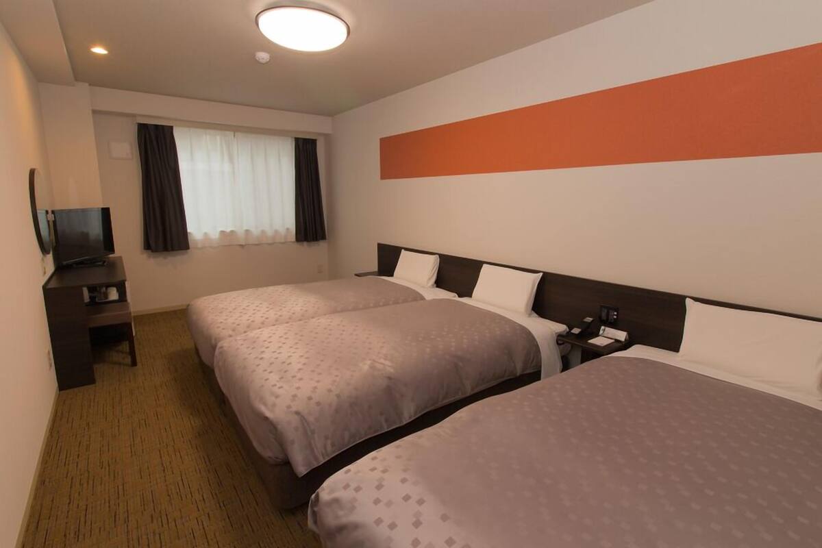 Une chambre d’hôtel avec deux lits, une télévision, un bureau et une fenêtre avec des rideaux.