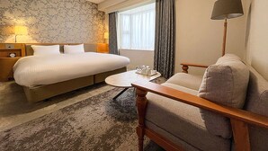 A hotel room with a large bed, a sofa, a small table, a lamp, and a window with curtains.